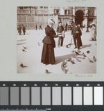 Black and white griny picture of an elegantly dressed woman feeding pigeons, two men standing a bit further watching her